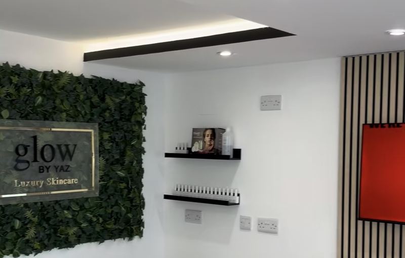 Inside Glow By Yaz in Bletchley: the Glow By Yaz Luxury Skincare logo on a green plant wall, beside display shelves and a fireplace