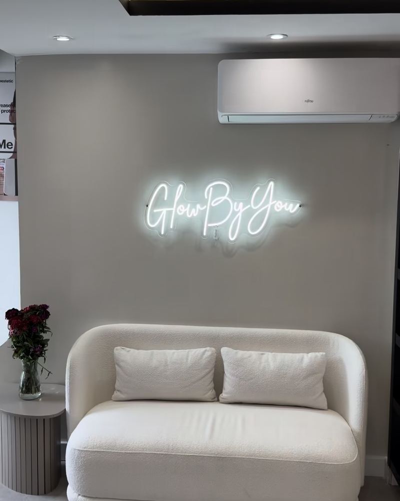 The waiting area at Glow By Yaz, Bletchley: a cream sofa beneath a Glow By You neon sign